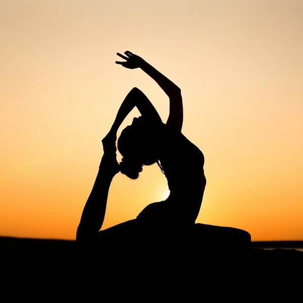 Silhouette of a person in a yoga warrior pose against a sunset.